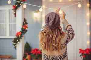 A woman installing holiday string lights on the porch as part of professional Holiday Lighting Services.