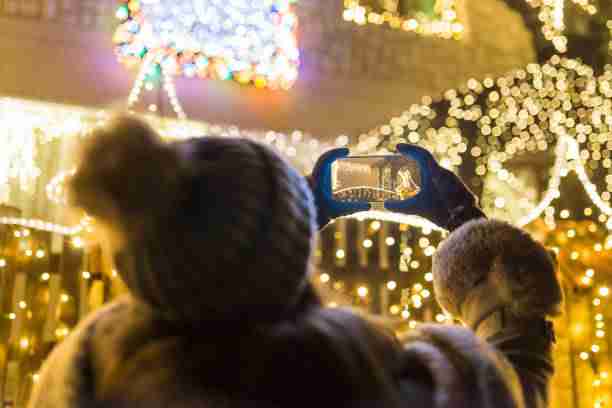 A person capturing the beauty of a glowing house adorned with holiday lights, emphasizing the magic of a professionally done holiday lights installation at 12900 Valley Branch Lane Suite 408 Farmers Branch, TX 75234.