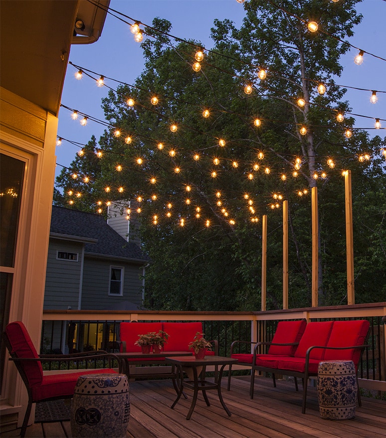 Deck of a home with light bulbs over a chairs and a coffee table. Patio Lighting Dallas, TX