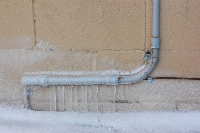 Frozen Pipes Downspout On Snowy Icy Ground Alley Block Wall. Winterization Dallas, TX