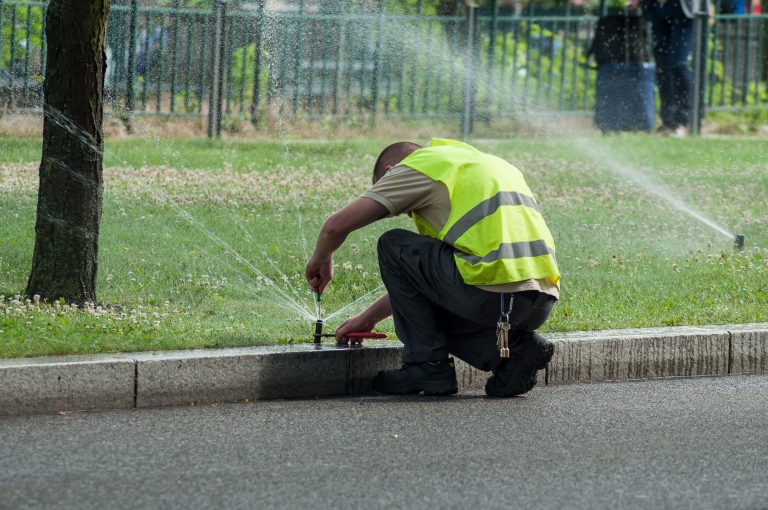 Worker in a reflective work jacket fixing a sprinkler. Sprinkler Repair Dallas County, TX